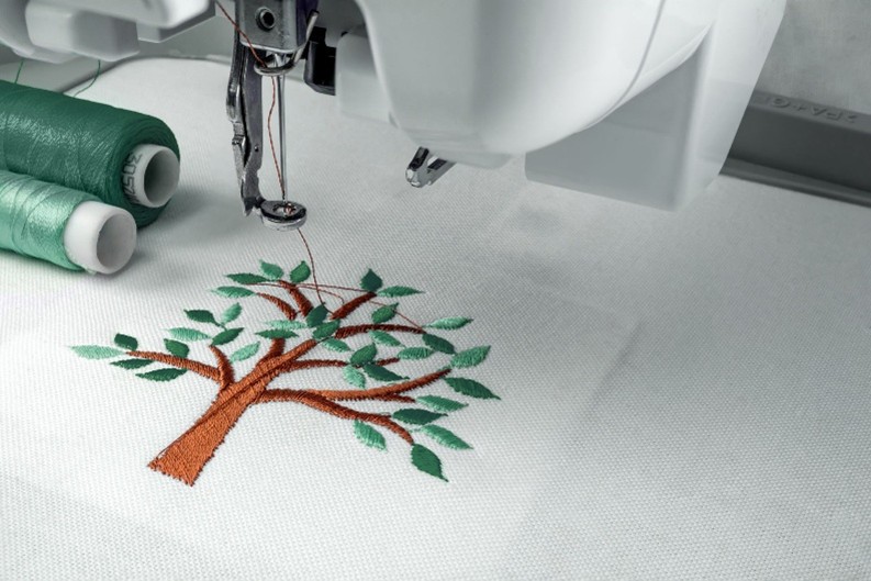Stickmaschine bestickt weißen Stoff mit einem Baum-Motiv aus grünem und braunem Garn.