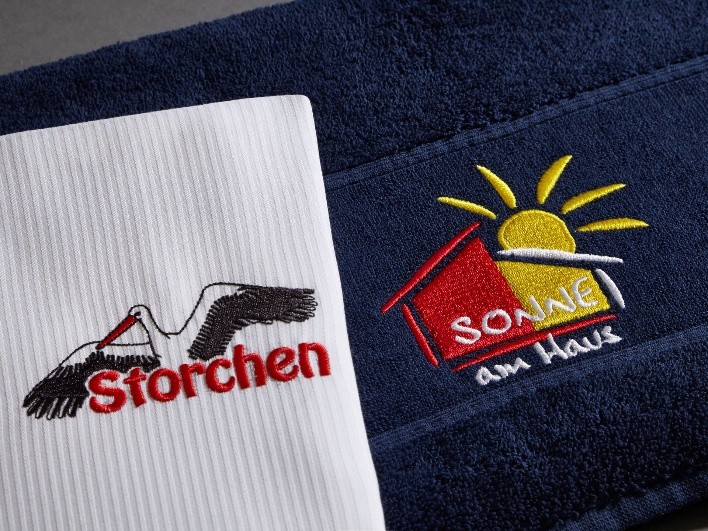 Zwei bestickte Textilien mit den Logo-Schriftzügen „Storchen“ und „SONNE am Haus“.