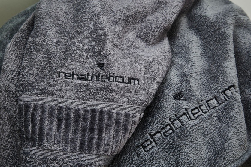 Detailansicht bestickter grauer Handtücher mit Logo-Schriftzug „rehathleticum“.