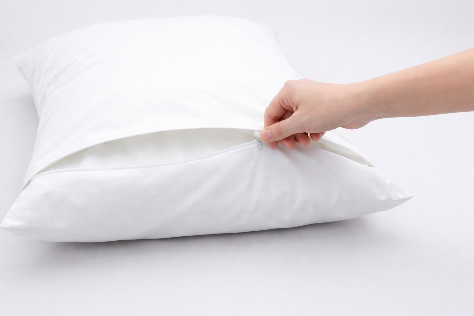 Hand schließt einen Reißverschluss an einem Kissen auf einem weißen Hintergrund.