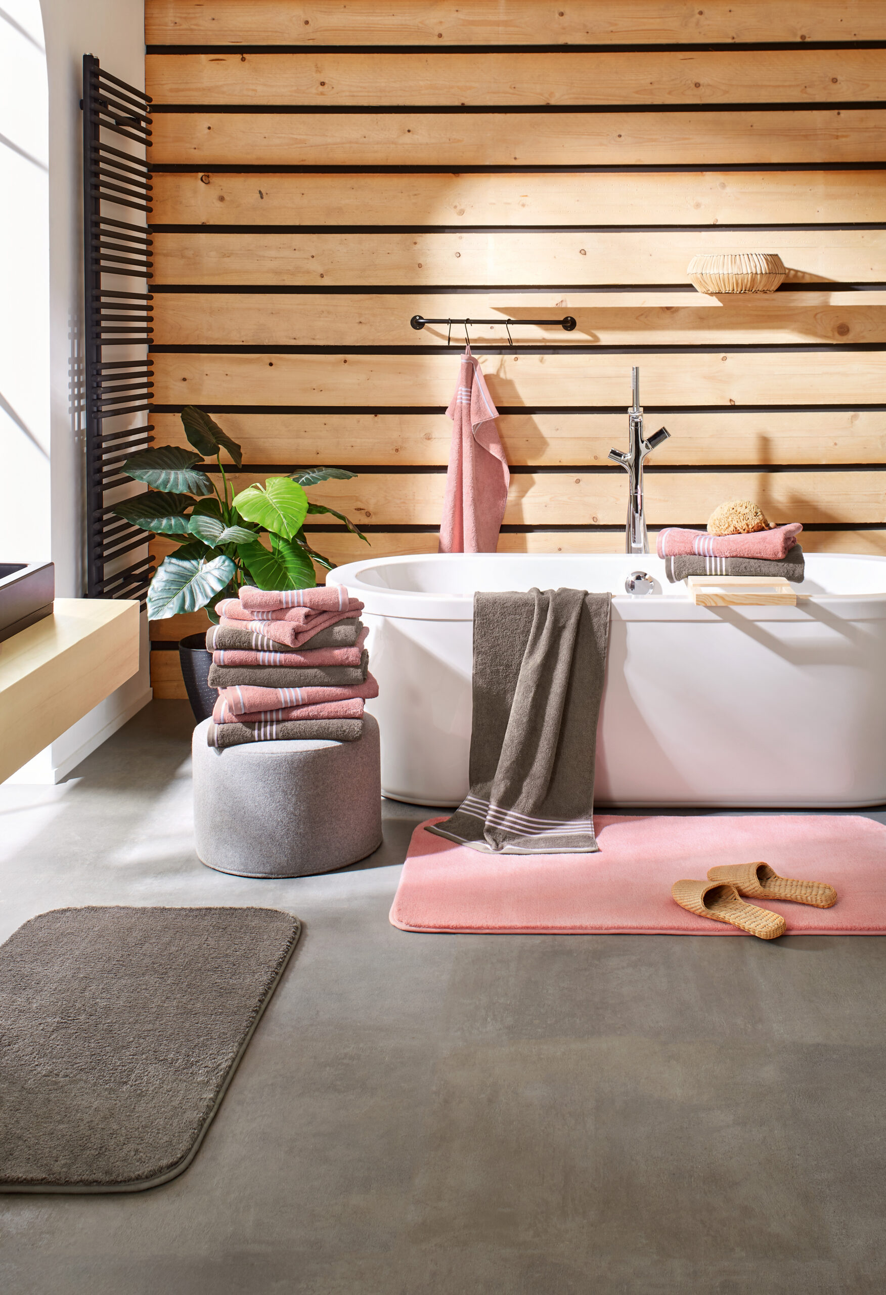 Freistehende Badewanne mit gefalteten Handtüchern und Badematten in Rosa und Grau.