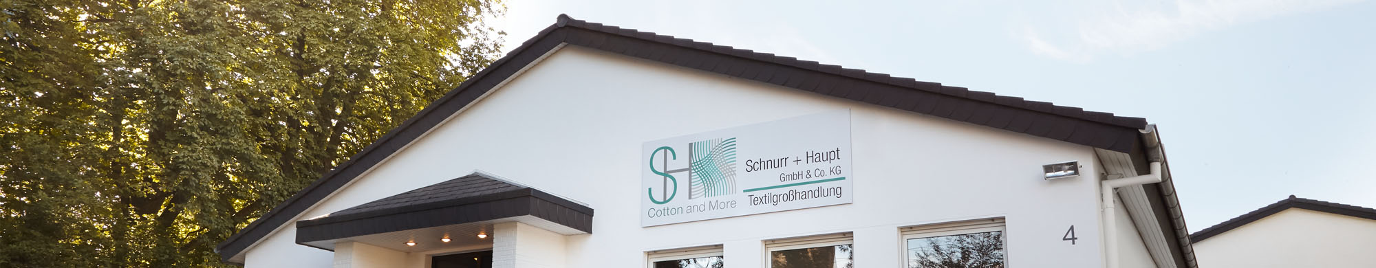 Gebäude zeigt Beschilderung mit Firmennamen, flankiert von Bäumen und blauem Himmel.