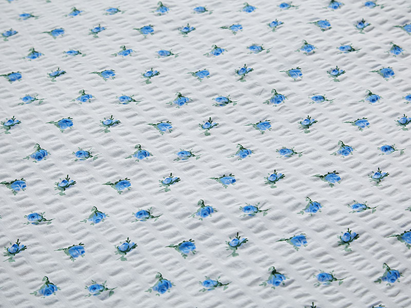 Detailansicht blauer Seersucker-Bettwäsche mit kleinen, regelmäßig angeordneten Rosenblüten auf weißem Hintergrund und typischer Stoffstruktur.
