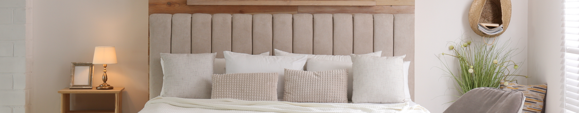 Bett mit beigen Kissen steht in einem hellen, gemütlich eingerichteten Schlafzimmer.