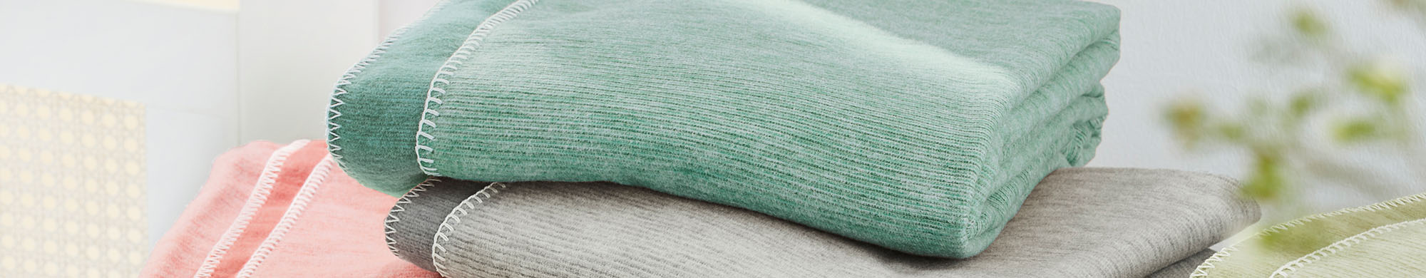 Drei gefaltete Decken liegen gestapelt aufeinander in einem beleuchteten Raum.