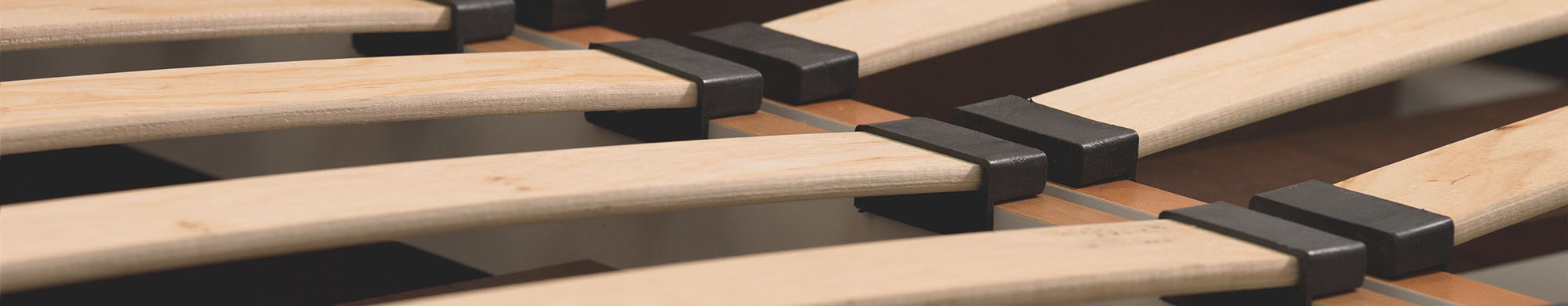 Nahaufnahme von Lattenrost. Holzlatten sind horizontal angeordnet, verbunden durch schwarze Kunststoffhalterungen in einem Bettrahmen.