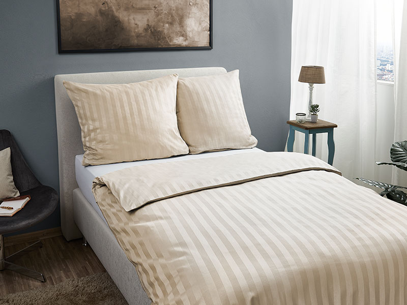 Hotel-Streifendamast Bettwäsche farbig Schlafzimmer mit cremefarbener Bettwäsche aus Streifendamast auf einem weißen Polsterbett, kombiniert mit modernen Möbeln und wohnlicher Dekoration.