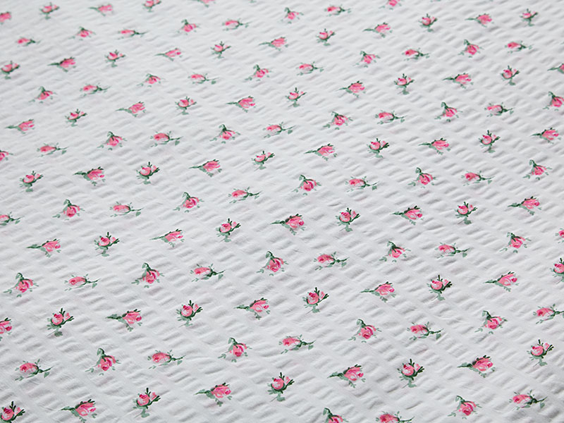 Detailansicht rosafarbener Seersucker-Bettwäsche mit kleinen, regelmäßig angeordneten Rosenblüten auf weißem Hintergrund und typischer Stoffstruktur.