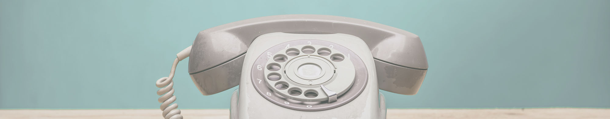 Ein graues Wählscheibentelefon steht auf einem Holztisch vor einer blauen Wand.