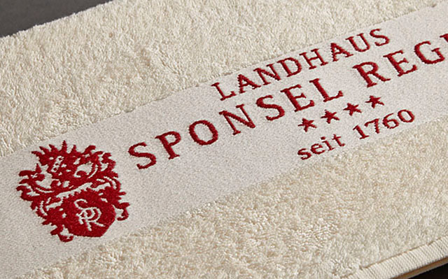 Ein Handtuch zeigt ein Wappen und Schriftzug auf cremefarbenem Stoff im Innenbereich.