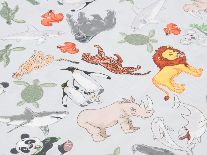 Nahaufnahme farbenfroher Kinderbettwäsche mit Tiermotiven wie Elefant und Giraffe auf weißem Hintergrund.