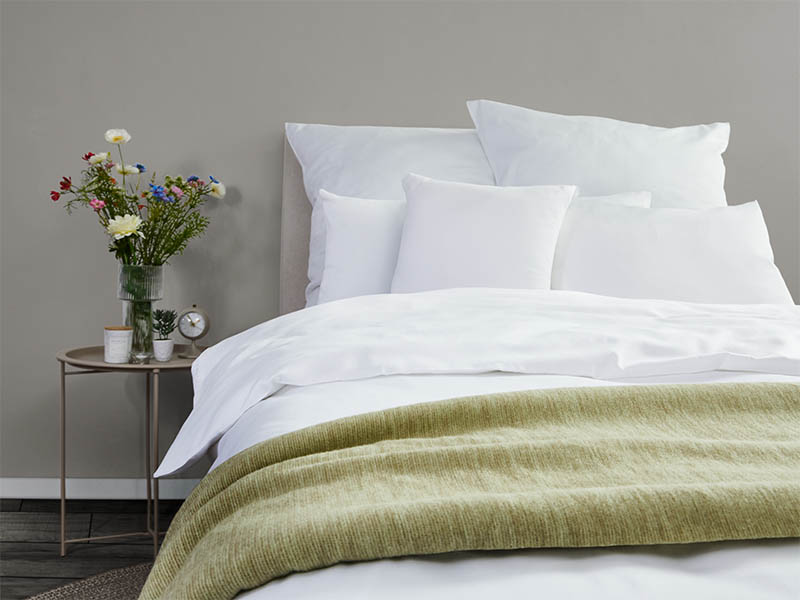 Satin-Bettwäsche Lynn | 140x210, weiß Blick auf ein modernes Bett mit weißer Bettwäsche und einer grünen Tagesdecke.