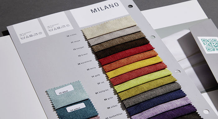 Stoffmuster zeigen verschiedene Farben auf einer Milano-Musterkarte, liegend auf einem Tisch.