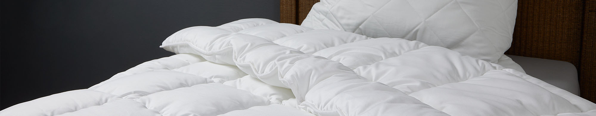 Eine weiße Decke und Kissen liegen auf einem Bett in einem dunklen Raum.