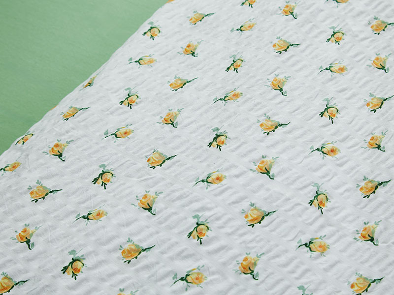 Detailansicht gelber Seersucker-Bettwäsche mit kleinen Rosenblüten auf weißem Hintergrund, daneben grüne Fläche als farblicher Kontrast.
