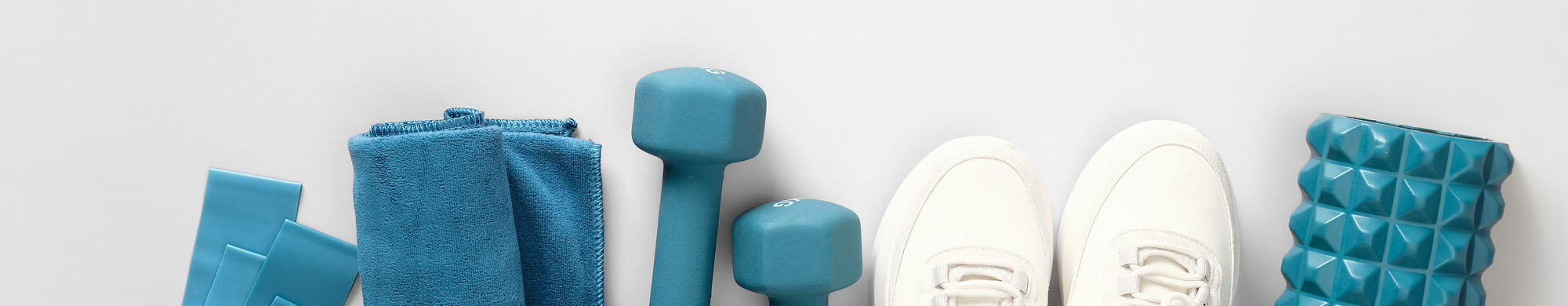 Hantel befindet sich neben Handtuch, Turnschuhen und Schaumstoffrolle auf hellgrauem Hintergrund.