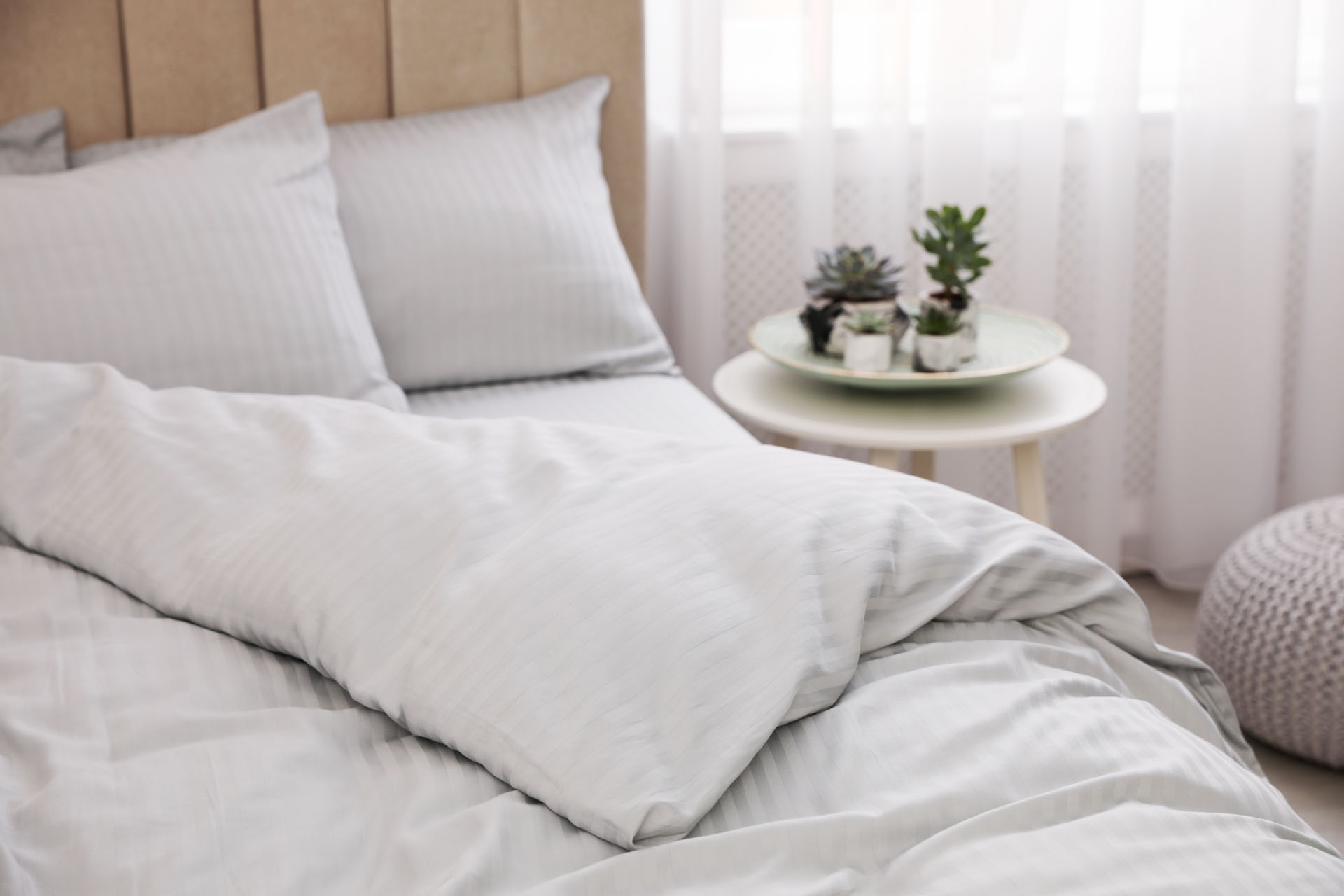 Ein weißes Bett, neben einem Tisch mit Pflanzen, steht in einem hellen Raum.