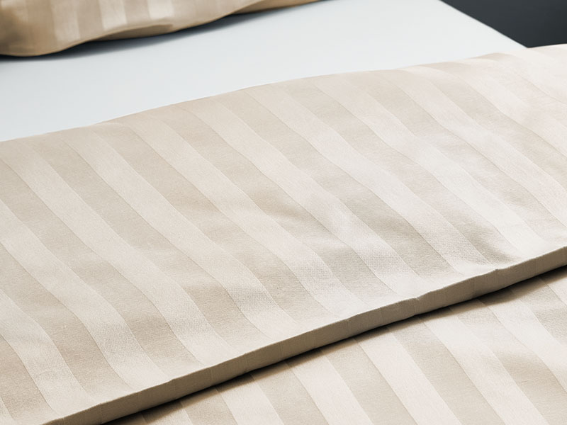 Hotel-Streifendamast Bettwäsche | 80x80, creme - Stück Nahaufnahme cremefarbener Streifendamast-Bettwäsche, die dezente Glanzstreifen und die hochwertige Webstruktur des Stoffes zeigt.