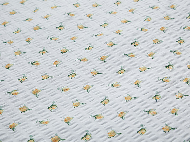Detailansicht gelber Seersucker-Bettwäsche mit kleinen, regelmäßig angeordneten Rosenblüten auf weißem Hintergrund und typischer Stoffstruktur.