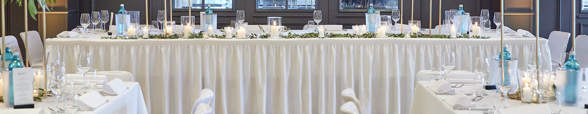 Tisch mit weißer Tischdecke und Kerzen, dekoriert für ein festliches Abendessen in einem Saal.