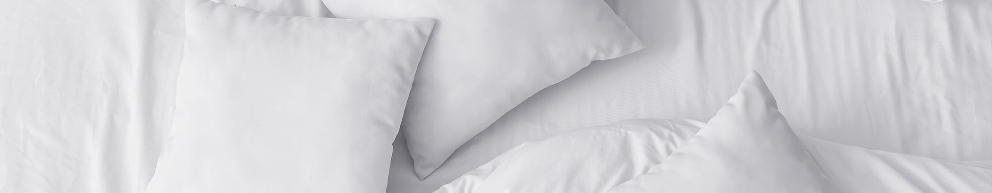 Weiße Kissen liegen ordentlich auf einem Bett mit glatter, weißer Bettwäsche.